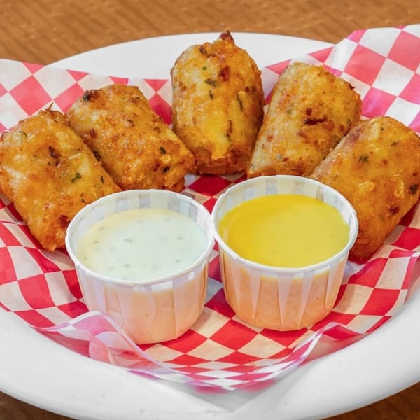Five golden-brown fried appetizers with two dipping sauces on a red and white checkered paper.