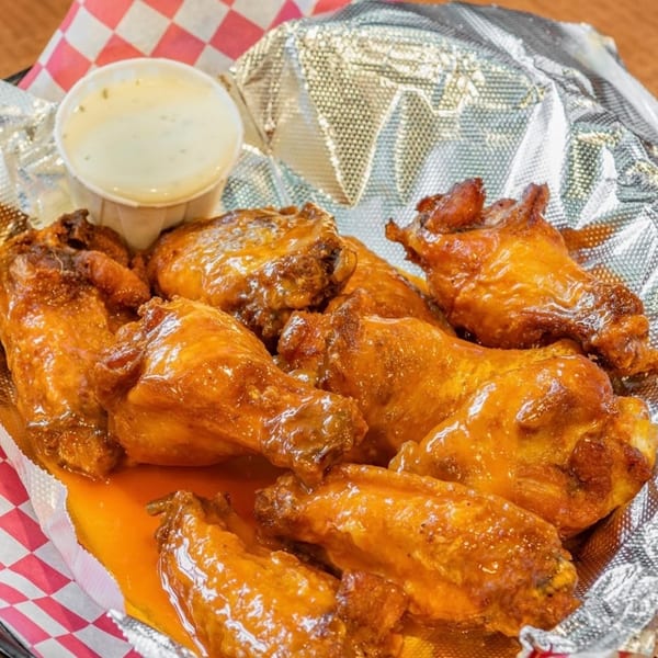 Armando's Grill & Pizzeria's buffalo wings, glistening with sauce, served in a foil-lined basket with ranch.