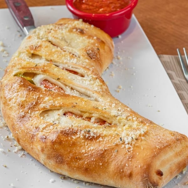 Golden-brown calzone with melted cheese and sauce, served with a side of marinara.